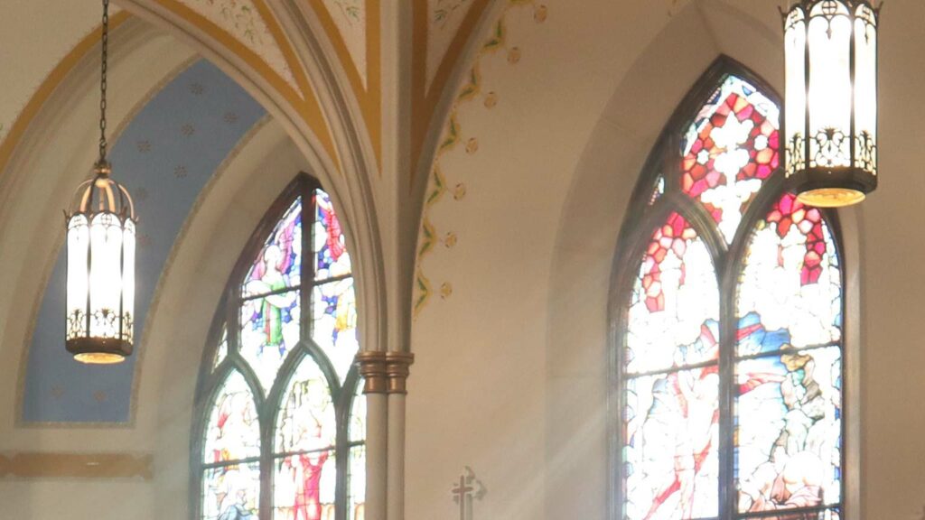 Fotografie von Buntfenstern und Lampen aus einem Innenraum einer Kirche.